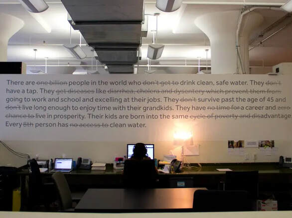 Person working at a desk at Charity: Water beneath a big printed message about the charity's work