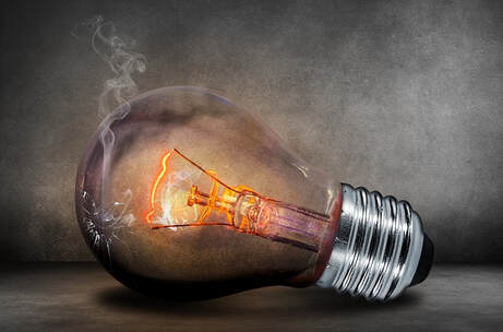 Lightbulb lying on its side with a crack in it and a small wisp of smoke coming out of the crack