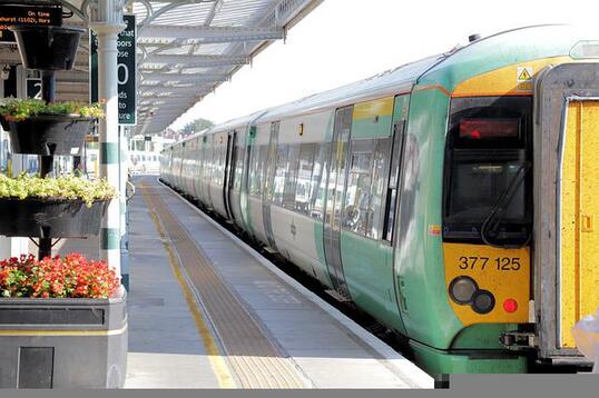 Photo of the back of a green, yellow and white passenger train, waiting to pull away from a UK rail platform 