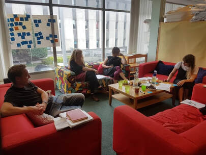 Group of participants sitting on sofas in our case for support workshop, with flipchart paper and colourful post-its displayed in the background